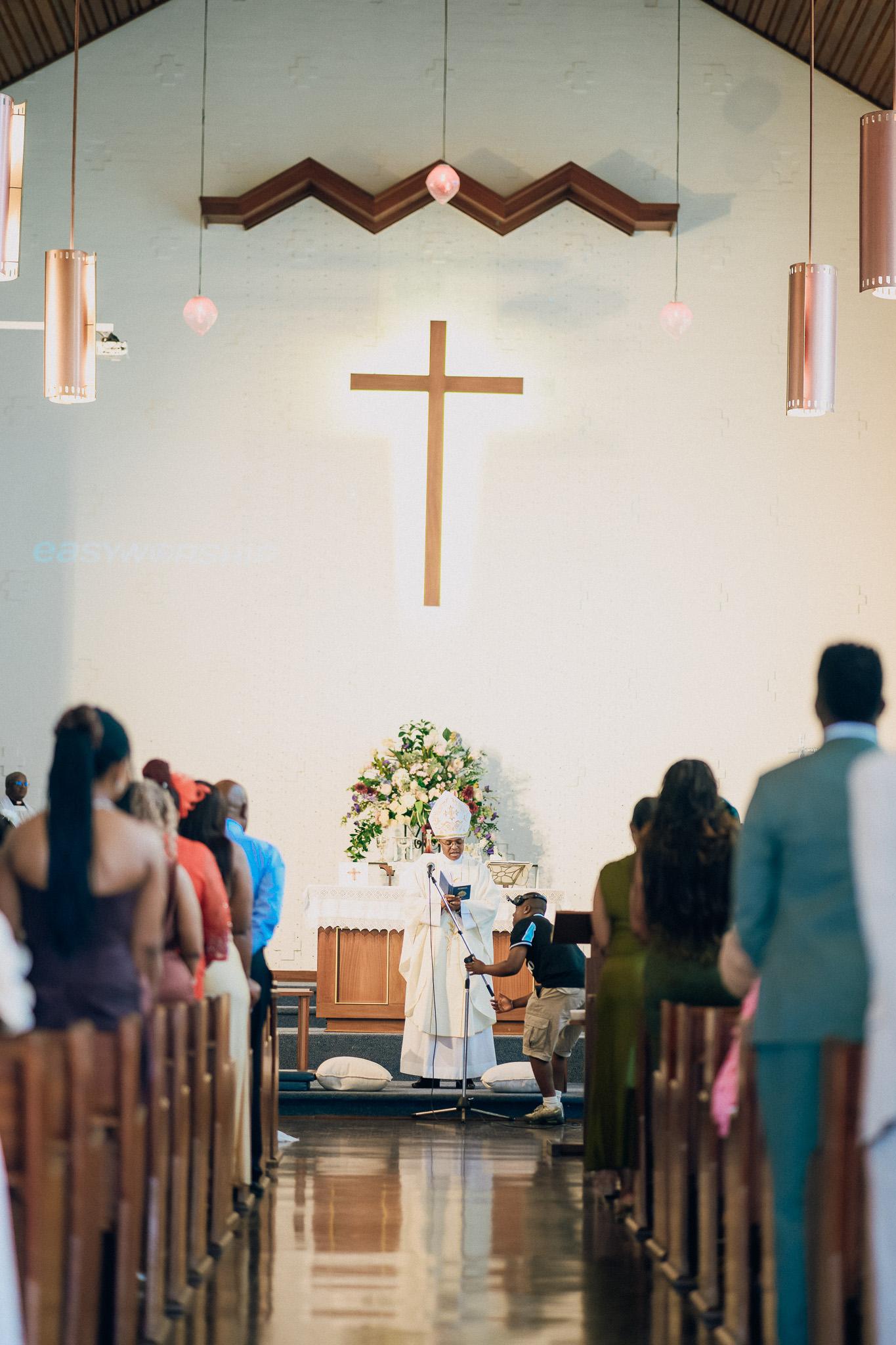 Wedding ceremony viewed down the church aisle beneath a cross.