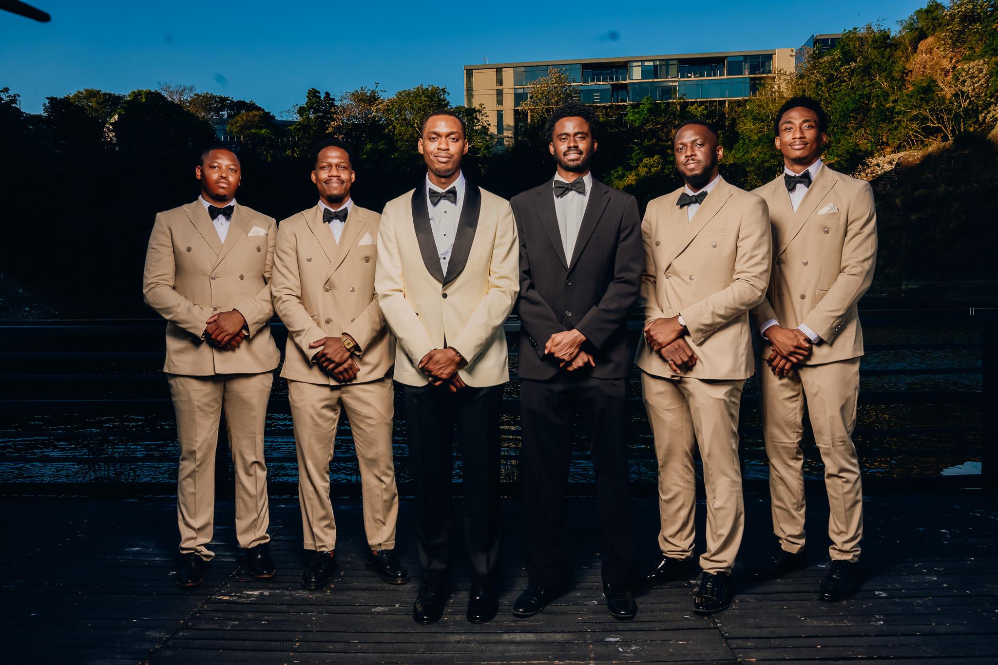 Groom with guests in cream and dark suits on an outdoor terrace.
